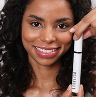 Una donna mostra con sicurezza un tubetto di mascara, mettendo in risalto il suo prodotto di bellezza con un sorriso luminoso.