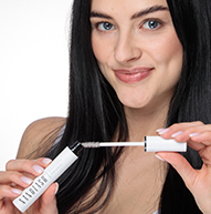 Una donna tiene elegantemente un tubetto di mascara Nanolash, mostrando la sua bellezza e fiducia in un ambiente elegante.