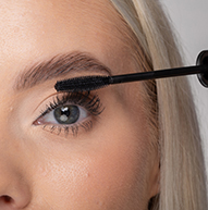 Una donna usa un pennello per mascara per applicare il mascara, migliorando abilmente le sue ciglia per un aspetto più drammatico.