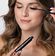 Una donna applica con attenzione il mascara per migliorare le sue ciglia, concentrandosi intensamente sulla sua routine di trucco.