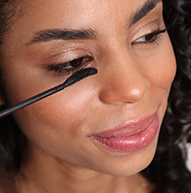Una donna applica il mascara al suo occhio, mostrando il suo processo di applicazione del trucco in un ambiente luminoso ed elegante.