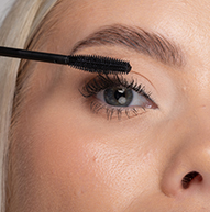 Una donna applica con cura il mascara alle sue ciglia usando un pennello per mascara, migliorando il suo trucco occhi con precisione.