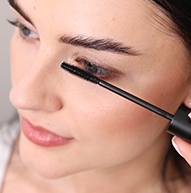 Una donna usa con abilità un pennello per mascara per applicare il mascara, concentrandosi sulle sue ciglia per ottenere un look definito.