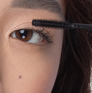 Una donna viene vista applicare il mascara con un pennello, concentrandosi sulle sue ciglia per ottenere un look definito ed elegante.